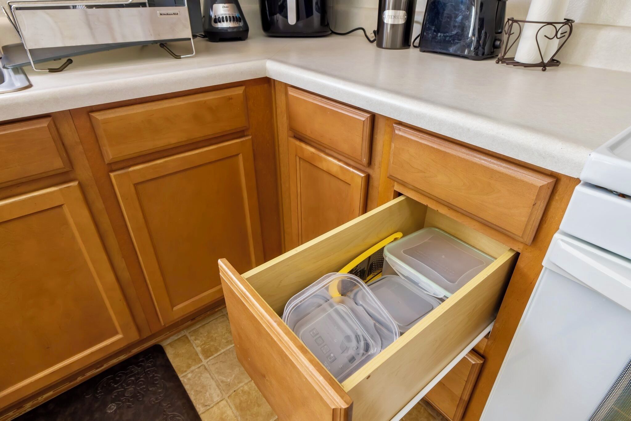 A kitchen with wooden cabinets, a countertop with appliances, and a drawer with storage containers.