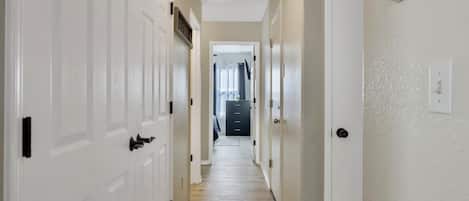 A hallway with white doors, a wooden floor, and a ceiling light fixture.