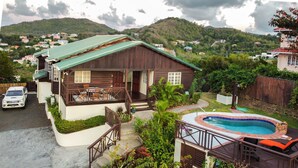A two-story house with a swimming pool, surrounded by lush greenery and hills in the background.