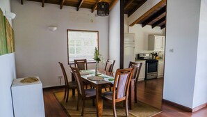 A dining area with a wooden table and chairs, a small white cabinet, and a window with blinds.