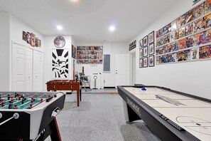 Una habitación con mesa de fútbolín, mesa de billar y una pared llena de cómics.