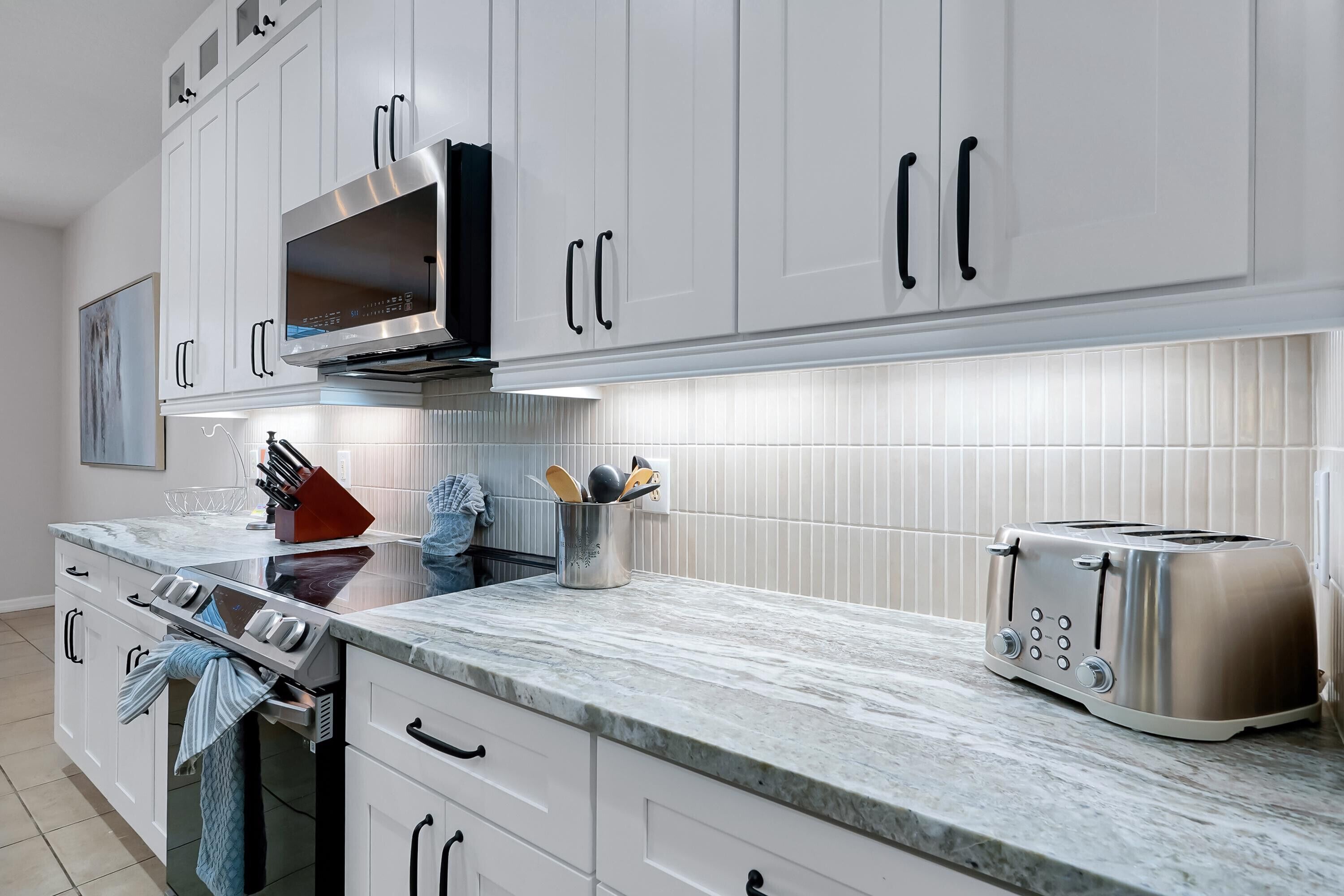A modern kitchen with white cabinets, a stainless steel range, a toaster, and a marble countertop.