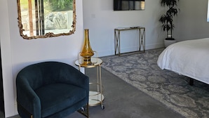 A modern bedroom with a large mirror, a TV, a bed, a sofa, and a small table with a lamp. - Hidden Hacienda King Room with Garden View (Temecula)