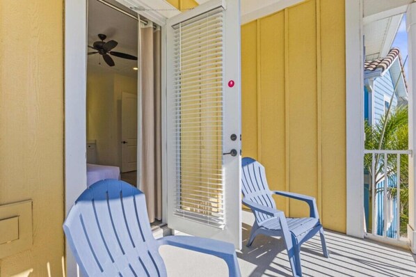 Un balcon avec deux chaises blanches, une porte avec une fenêtre et un ventilateur de plafond.