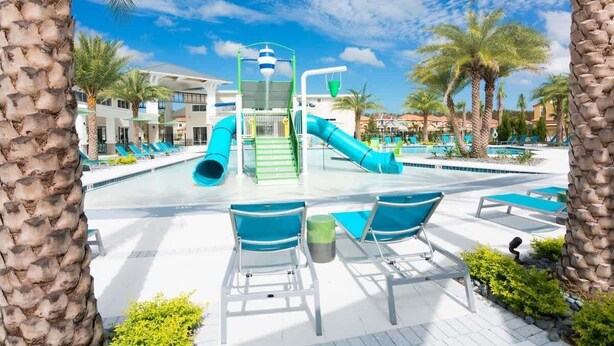 A pool area with a water slide, lounge chairs, and palm trees.