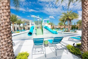 Un espace piscine doté d’un toboggan, de chaises longues et de palmiers.