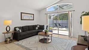 A modern living room with a sectional sofa, a coffee table, a lamp, and a large window with curtains.