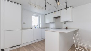 A modern kitchen with white cabinetry, a central island, and pendant lighting. - Belgravia 2 BR Hideaway with Balcony (London)