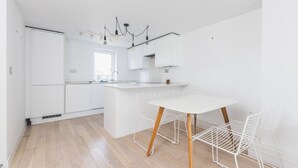A modern kitchen with white cabinetry, a central island, and a dining area with a white table and chairs. - Belgravia 2 BR Hideaway with Balcony (London)