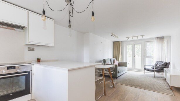 A modern kitchen with a built-in oven, a dining area with a table and chairs, and a seating area with a sofa and a chair. - Belgravia 2 BR Hideaway with Balcony (London)