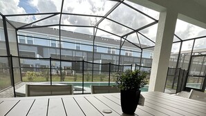 A covered outdoor seating area with a table and chairs, a potted plant, and a view of a residential building through a glass enclosure. - Last Minute Disney! Private Pool, Hot Tub & Themed Bedrooms. Book Now! #119785 (Orlando)
