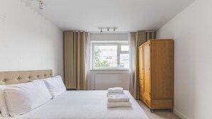 A bedroom with a bed, a wooden wardrobe, a window with curtains, and a radiator.