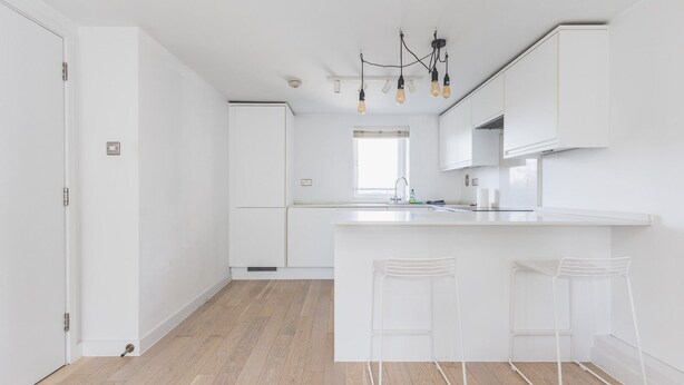 A modern kitchen with white cabinetry, a central island with bar stools, and a pendant light fixture.
