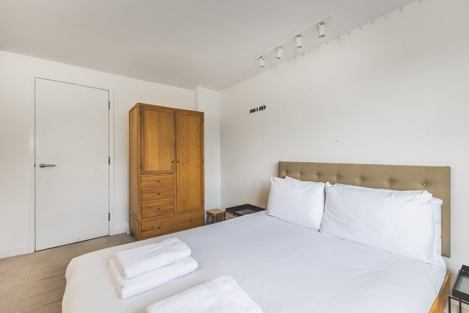 A bedroom with a bed, a wooden wardrobe, a nightstand, and a wall-mounted light fixture.