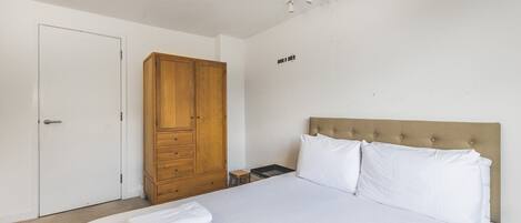 A bedroom with a bed, a wooden wardrobe, a nightstand, and a wall-mounted light fixture.