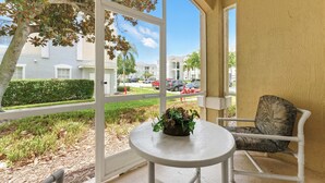 En balkon med et hvidt bord og en stol, en potteplante og udsigt over et boligområde med bygninger og parkerede biler.