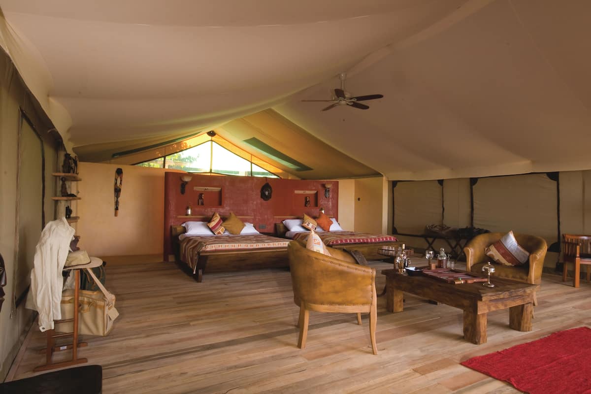 A spacious room with a high ceiling, wooden flooring, a large bed with multiple pillows, a wooden coffee table, and a ceiling fan.