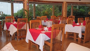 A restaurant with wooden tables and chairs, red tablecloths, and a view of greenery outside. - Mara Engai Wilderness Lodge (Nairobi)