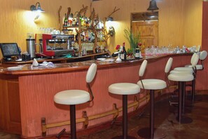 A bar area with a counter, stools, a cash register, and a variety of bottles and glasses. - Mara Engai Wilderness Lodge (Nairobi)