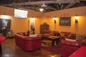 A cozy living room with red leather sofas, a wooden coffee table, and a flat-screen TV mounted on the wall. - Mara Engai Wilderness Lodge (Nairobi)