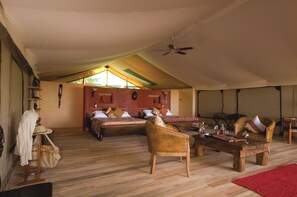 A spacious room with a high ceiling, wooden flooring, a large bed with multiple pillows, a wooden coffee table, and a ceiling fan.