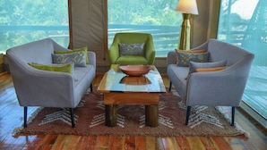 A room with two grey armchairs, a green armchair, a wooden coffee table with a bowl, and a lamp. - Mara Engai Wilderness Lodge (Nairobi)