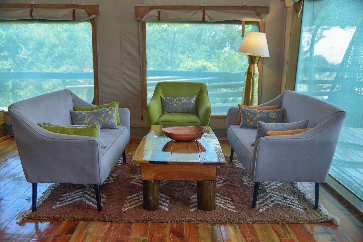A room with two grey armchairs, a green armchair, a wooden coffee table with a bowl, and a lamp.