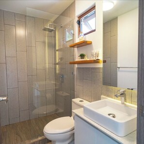 Ein modernes Badezimmer mit einer gläsernen Duschkabine, einer weißen Toilette und einem Waschbecken mit Spiegel darüber.
