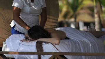Sessão de massagem em um quarto de madeira com telhado de palha, transmitindo um ambiente natural e tranquilo.