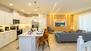 A modern kitchen with white cabinets, a central island, and a dining area with chairs.