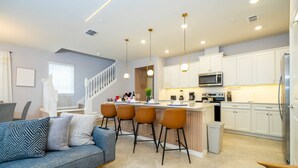A modern kitchen with white cabinets, a central island with bar stools, a microwave, and a refrigerator.