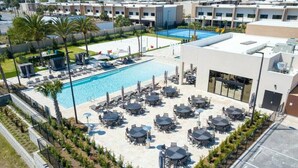 A rooftop pool area with multiple lounge chairs and tables, surrounded by a low fence and greenery.
