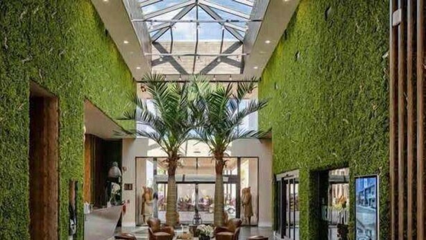 A spacious lobby with a high ceiling, green walls, and a central seating area with leather chairs and tables.
