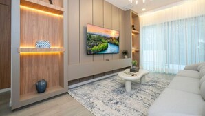 Un salon moderne avec un téléviseur à écran plat, des étagères en bois, un canapé blanc et un tapis à motifs.