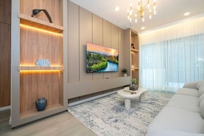 A modern living room with a flat-screen TV, wooden shelving, a white sofa, and a patterned rug.