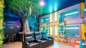 Une chambre avec un grand décor mural représentant un arbre, des lits superposés et un coin salon avec des chaises.