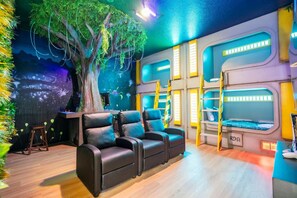 A room with a large tree mural, bunk beds, and a seating area with chairs.