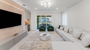 Ein modernes Wohnzimmer mit Flachbildfernseher, einer Couch, einem Couchtisch und einem gemusterten Teppich.