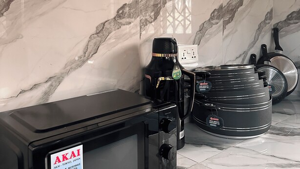 Cucina con forno a microonde da 20 litri, macchina per il caffè e pentole e padelle nere su un piano di lavoro in marmo.