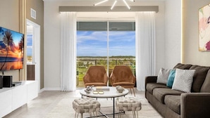 A modern living room with a large window, a flat-screen TV, a sofa, two armchairs, and a coffee table. - Last Minute Disney Getaway! Themed Bedrooms & Private Balcony. Book Now! #150901 (Orlando)