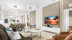 A modern living room with a large flat-screen TV, a sofa, chairs, and a dining area in the background. - Last Minute Disney Getaway! Themed Bedrooms & Private Balcony. Book Now! #150901 (Orlando)