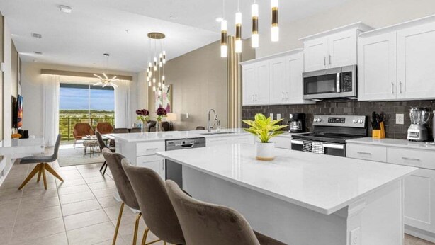 A modern kitchen with white cabinetry, a large island, and pendant lighting. - Last Minute Disney Getaway! Themed Bedrooms & Private Balcony. Book Now! #150901 (Orlando)
