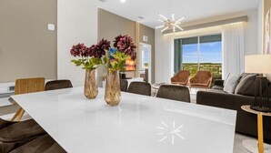 A modern dining area with a white table, two vases with flowers, and a contemporary chandelier. - Last Minute Disney Getaway! Themed Bedrooms & Private Balcony. Book Now! #150901 (Orlando)