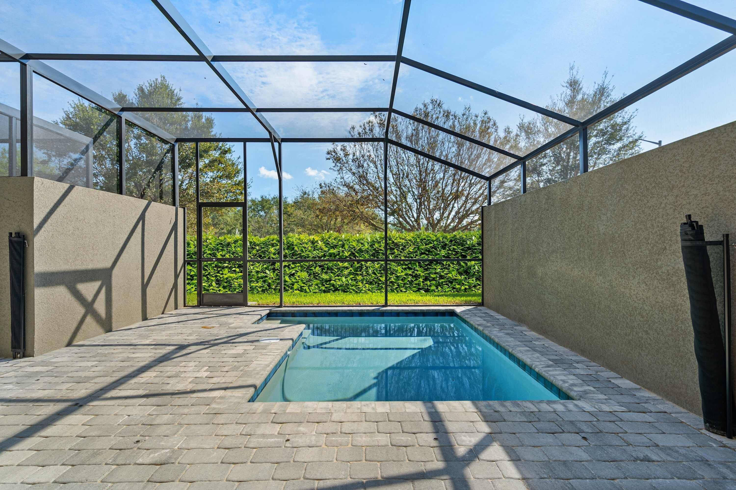 Une piscine dotée d’une enceinte en verre, entourée d’une terrasse dallée et d’une haie.