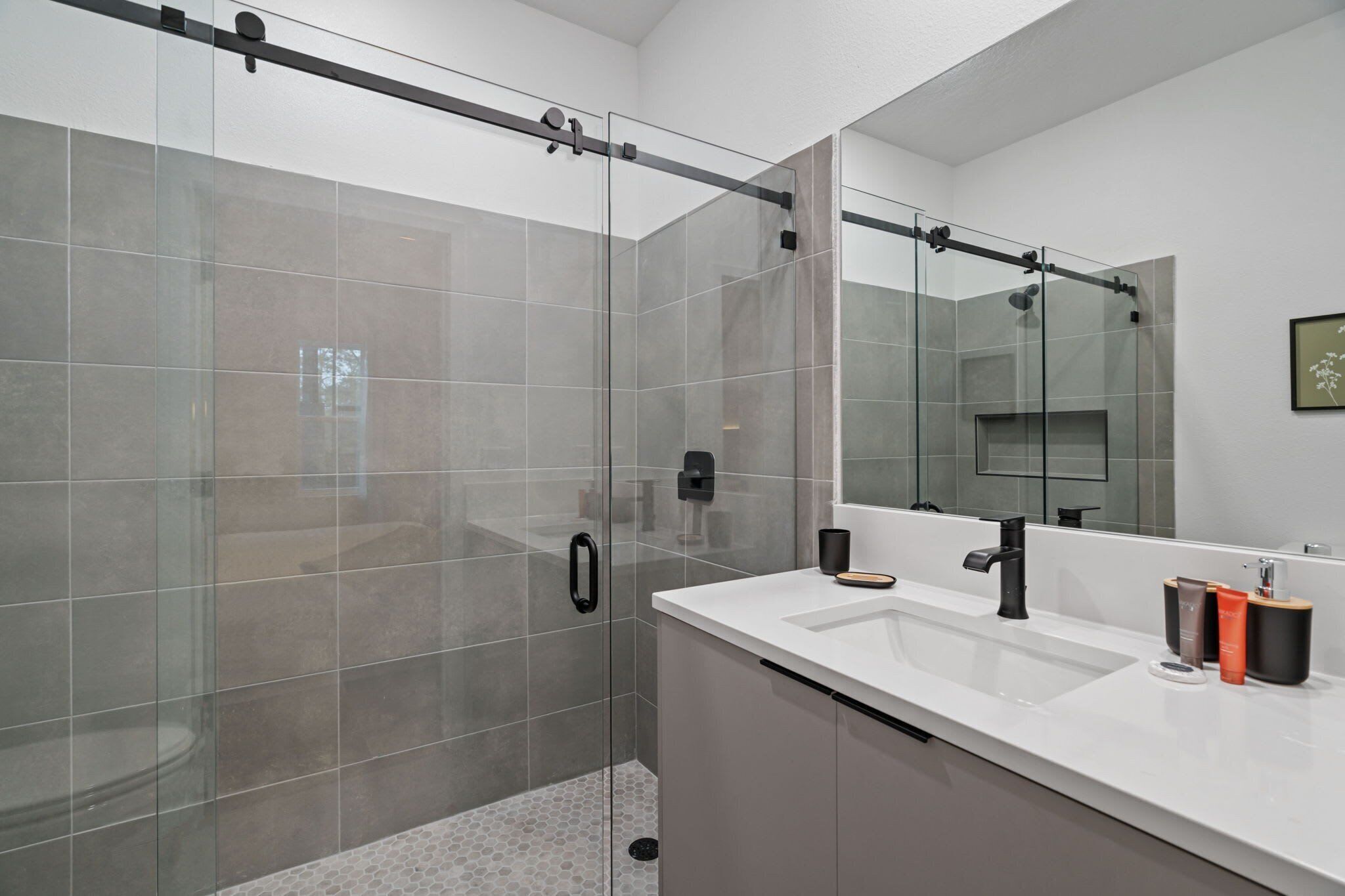 A modern bathroom with a glass-enclosed shower, a large mirror, and a white countertop with toiletries.