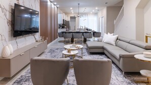 A modern living room with a large flat-screen TV, a sectional sofa, and a dining area with a round table and chairs.