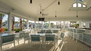 An outdoor dining area with white tables and chairs, a bar, and a ceiling fan.