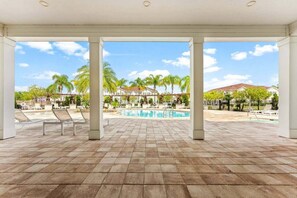 Un espacio al aire libre cubierto con piscina, sillas de descanso y vistas a un barrio residencial.