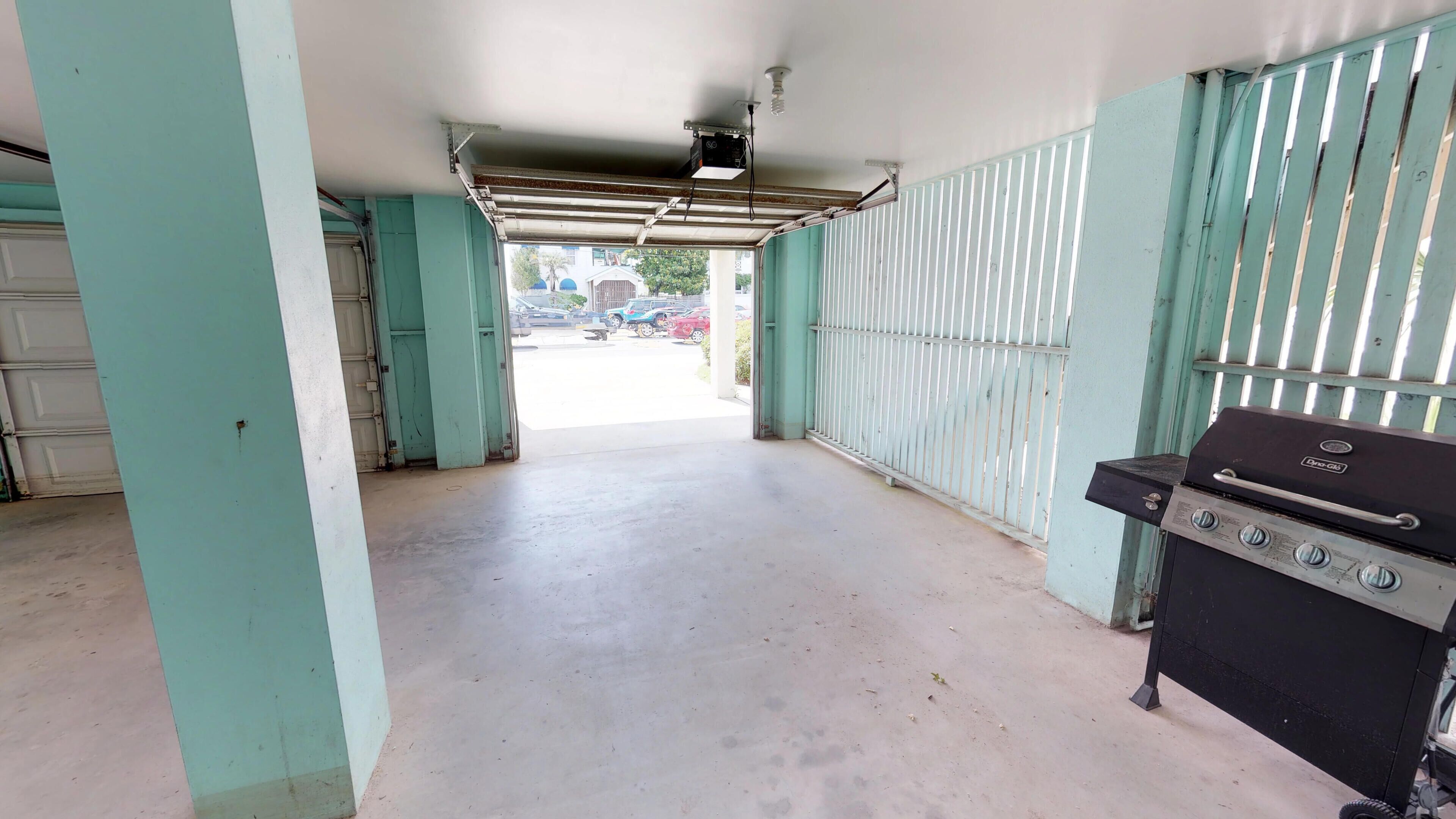A covered outdoor area with a barbecue grill, a garage door, and a metal fence.