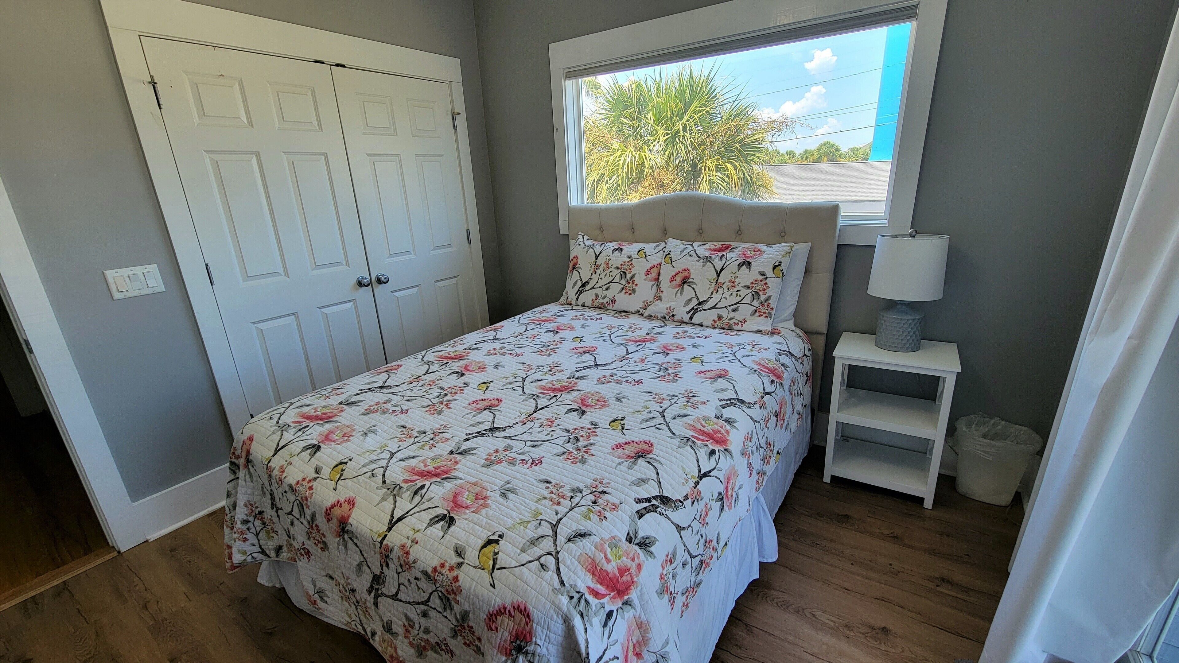 A bedroom with a bed, a window, a wardrobe, and a bedside table.